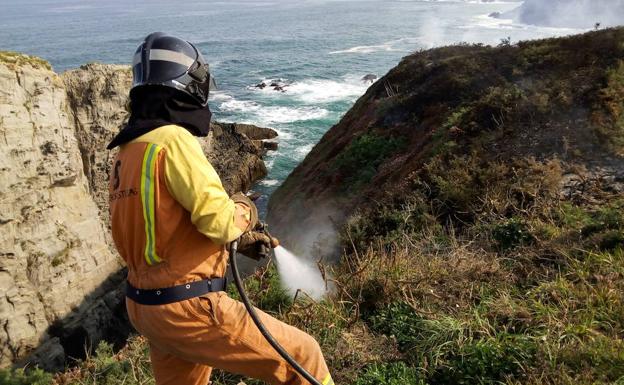 Un bombero trabaja en las labores de extinción de un incendio en la senda costera de Navia.