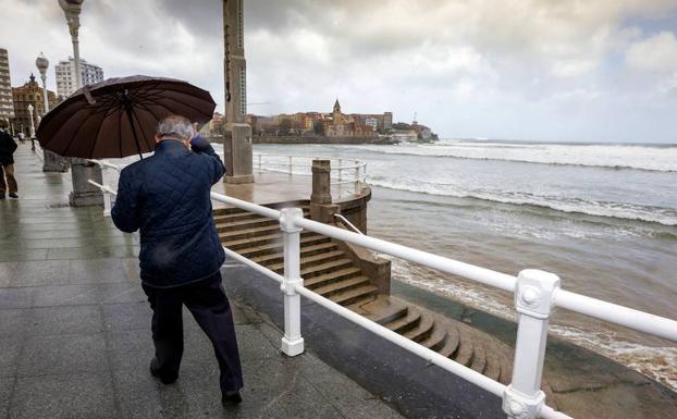 Un hombre se protege en Gijón de la lluvia y el viento en el mes de marzo. /EFE