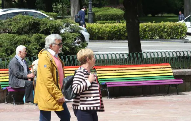 Dos señores pasean delante de los bancos arcoíris. / ALEX PIÑA