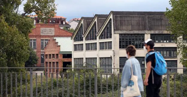 Una pareja camina por delante de la Escuela de Artes y Oficios y la nave de Cañones en La Vega. / ALEX PIÑA