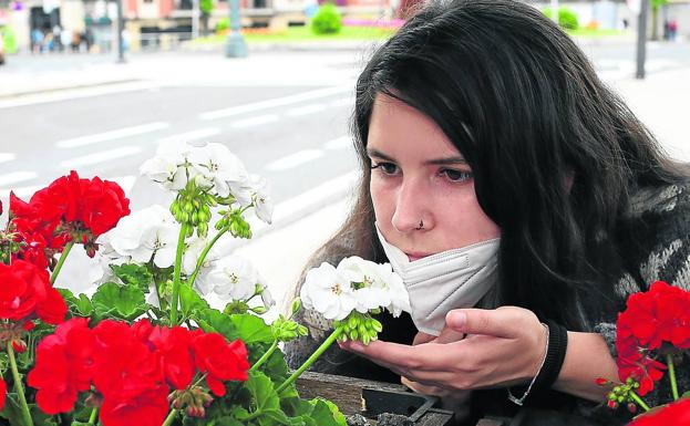 Una joven se retira la mascarilla para oler una flor en un jardín./r. c.